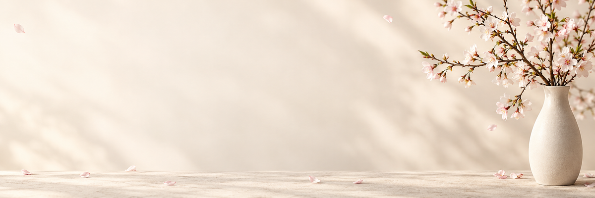 Natural cherry blossom branches in an ivory vase with scattered pink petals